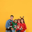 © New Africa - Family in Christmas sweaters and festive accessories on yellow background