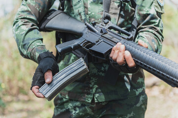 Army soldier holding a gun assembling a bullet into the gun magazine .