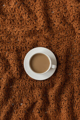 Wall Mural - Flatlay cup of coffee on brown crumpled knitted traditional woolen textile cloth texture. Fashion pattern. Flat lay, top view.