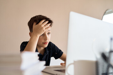 Smart looking boy doing his homework and look at computer notebook at home due to Covid-19 pandemic and social distancing, New normal, Remote class. High quality photo