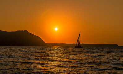 Wall Mural - A yacht of the island of Thirasia, Santorini silhouetted by the setting sun on a summers evening
