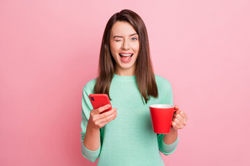 Sticker - Portrait of attractive cheerful flirty glad girl drinking tea using gadget winking isolated over pink pastel color background