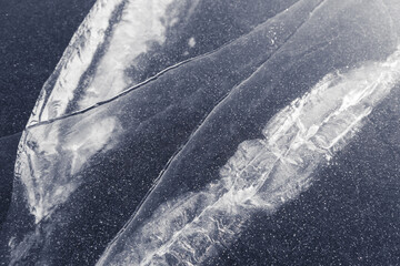 texture of stripes and cracks on a thick layer of ice of a lake or river. white cracks dark blue background