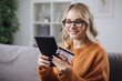 © Kuz Production - Happy young woman in eyeglasses using digital tablet and credit card for online shopping while staying at home. Concept of modern technology.