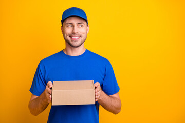 Photo of handsome guy arms hold package wear hat look empty space isolated on yellow color background