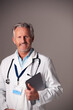 © Monkey Business - Studio Portrait Of Mature Male Doctor In White Coat Using Digital Tablet Against Grey Background