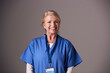© Monkey Business - Studio Portrait Of Mature Female Nurse Wearing Scrubs Standing Against Grey Background