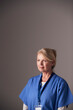© Monkey Business - Studio Portrait Of Mature Female Nurse Wearing Scrubs Standing Against Grey Background