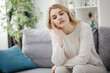 © Kuz Production - Tired young woman with hairstyle sitting on grey sofa with closed eyes. Bored lady in white clothing sitting at home during leisure time.