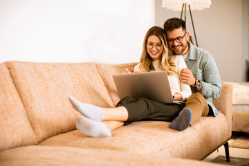 Young couple using laptop together while sitting on sofa at home