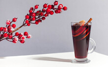 Mulled Wine In A Glass With A Stick Of Cinnamon, Branch With Red Winter Berries. Trendy, The Photo With The Hard Light.