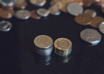 Two stack New sterling pound coins with blurry penny background, British money on table, Selective focus GBP coins on the floor in dark light, Business and financial for money saving or investment