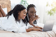 © Prostock-studio - Happy black women in bathrobes using laptop at home, websurfing