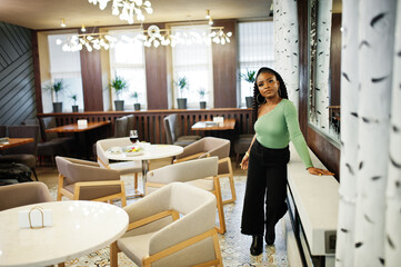 Portrait of attractive young african american woman wearing in green sweater and black jeans pose at restaurant.