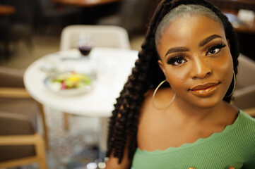 Portrait of attractive young african american woman wearing in green sweater posed at restaurant.