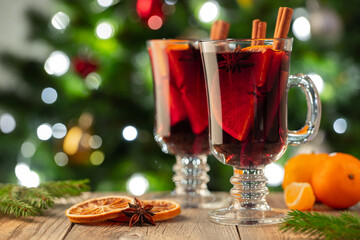 Two glass of christmas mulled wine or gluhwein with spices and orange slices on rustic table against the Christmas tree. Traditional drink on winter holiday