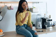 © nenetus - Pretty happy young woman eating yogurt while smiling thinking on her things sitting on the kitchen at home.