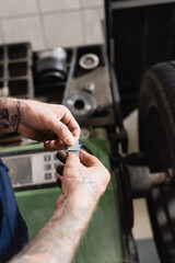 partial of mechanic removing metallic balancing plate from adhesive stripe near balance control machine on blurred background