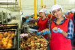 Smiling Latina woman worker standing in fruits industrial production facility holding ripe peaches