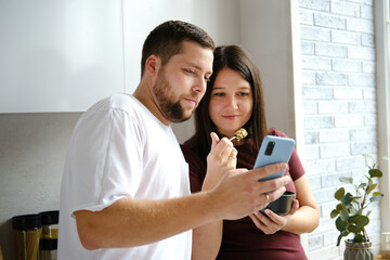 Happy young couple looking at smartphone while having breakfast at home