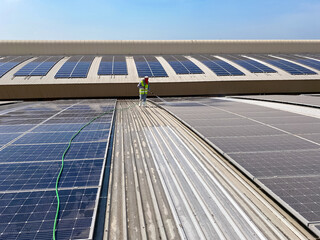 Young worker cleaning solar panels on the roof of a large industrial building or a warehouse.