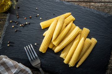 Wall Mural - Pickled young baby corn cobs on black stone cutting board.