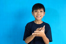 Asian Boy Clapping And Applauding Happy And Joyful, Smiling Proud Hands Together On Blue Background, Copy Space