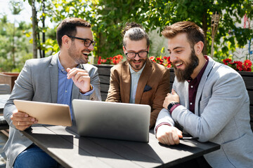 Positive successful business specialists discussing plan with laptop outdoors.