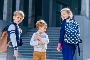 back view of three schoolchildren standing near their school. two boys and girl in uniform and backp