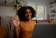© StratfordProductions - Cheerful african woman relaxing on couch waving hand while on video call using laptop and earphones