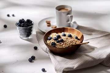 Poster - food, eating and breakfast concept - oatmeal in wooden bowl with blueberries and spoon, cup of coffee on kitchen towel