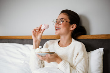 Cheerful girl gesturing and using laptop while sitting in bad