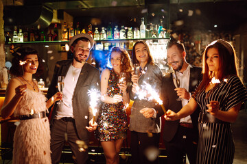 Group of happy people holding sparklers at the party. Young friends clinking glasses of champagne and enjoying new years eve with fireworks. Party, celebration, holidays concept.