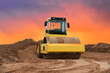Vibration single-cylinder road roller on amazing sunset background. Soil Compactor for leveling ground for the foundation and on road construction. Road compaction equipment at construction site