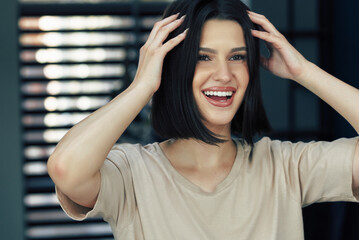 Canvas Print - A positive brunette girl has a joyful expression during arranges her hair. Happy young woman looking to the mirror and making hairstyle.