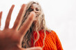 © iuricazac - Bottom view of a joyful young woman smiling in an orange sweater with her palm's hand out of focus in front of the camera, posing on the sky background. Pretty female playing outdoors.