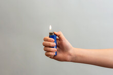 The Girl Wrapped Her Hand Around The Lighter And Lit Her Finger On A Gray Background.