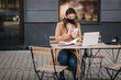 © Aleksandr - Young female in black face mask sitting on terrace in cafe during quarantine. Business woman working outdoos in quarantine. Woman speak by the phone. Covid-19