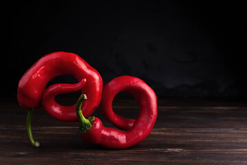 Two red hot twisted peppers on a dark wooden background, copy space, closeup