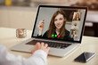 © Roman Tyukin - A laptop screen view of the telecommunications application during an online meeting over a man's shoulder. Back view of a man who is working remotely on a video conference on a computer from home.