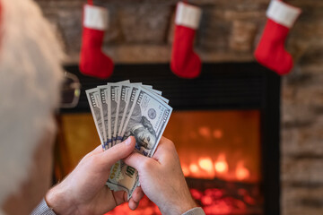 Man counting american dollars sitting near christmas tree and fireplace. Spending money on gift at christmas time. concept. Back view.