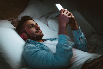 Young man using smart phone mobile - Millennial guy with cellphone lying on bed at home - Technology and people concept