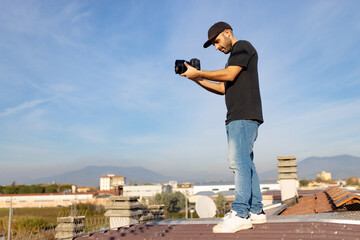 Wall Mural - Caucasian videographer filming with cinema video dslr on the rooftop during a sunny day, professional video, videographer in event. Cinema lens. Space for graphics and writing