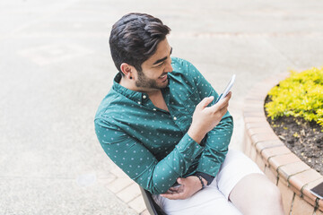 Wall Mural - Top view closeup of a Hispanic man standing outside and smiling with his phone in his hands