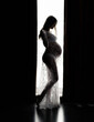 Silhouette of a beautiful pregnant woman near the window. Beauty and tender motherhood.