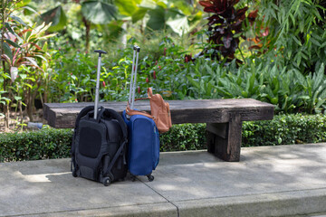 luggages for travelers outdoors. Summer vacation and travel concept. two travel bags- blue and black on wheels near the bench outside. background vegetation