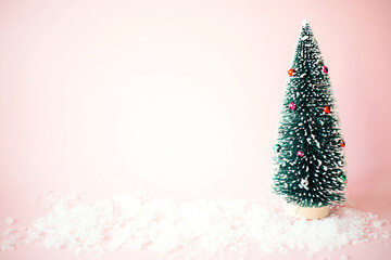toy little christmas tree on a pink background with snow.