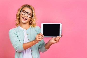 Happy attractive little kid teen girl holding a blank tablet in her hands so that the blank screen with white copyspace. Isolated over pink background.