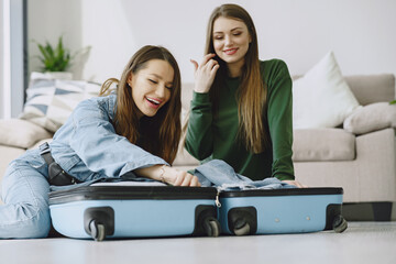 Excited women trying to close full suitcase. Packing luggage. Travel, lifestyle and vacation concept.