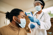 Black Man With Face Mask Getting His Temperature Measured By A Doctor During Home Visit.